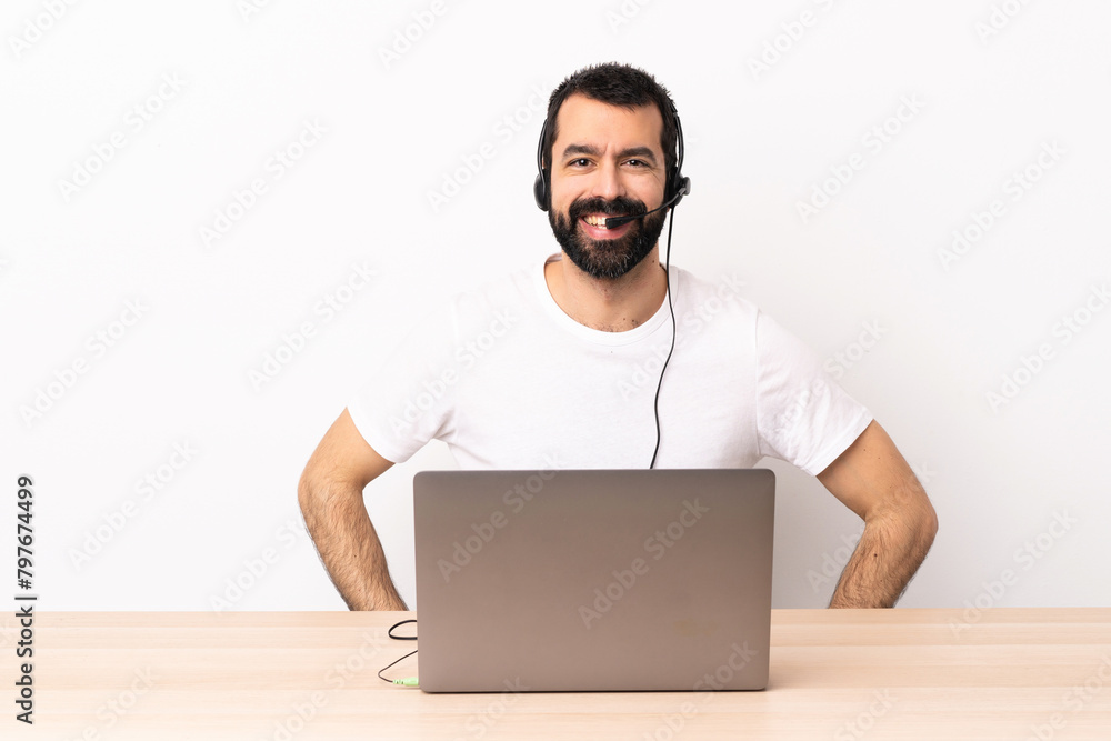 Telemarketer caucasian man working with a headset and with laptop posing with arms at hip and smiling. Telemarketer caucasian man working with a headset and with laptop posing with arms at hip and smiling.