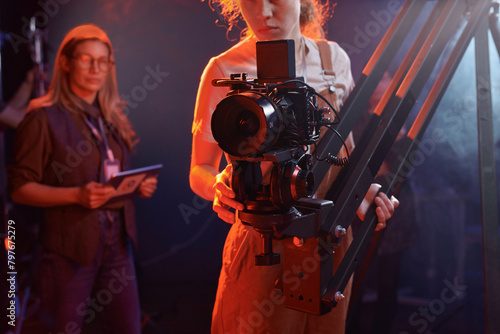 Cropped shot of young woman operating video camera on rig in studio with neon lights copy space