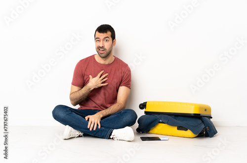 Caucasian handsome man with a suitcase full of clothes sitting on the floor at indoors pointing to oneself © luismolinero