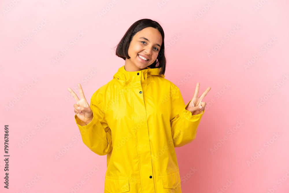 Young latin woman wearing a rainproof coat over isolated background showing victory sign with both hands Young latin woman wearing a rainproof coat over isolated background showing victory sign with both hands