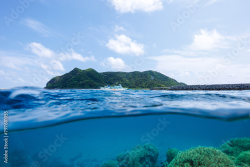 素晴らしいサンゴ礁の水面から見る、慶良間諸島フェリーのクイーンざまみ３世号と慶留間島の美しい半水面撮影。 圧倒的に大規模な素晴らしく美しいサンゴ礁。沖縄県島尻郡座間味村阿嘉島の阿嘉ビーチにて。 2021年4月28日水中撮影。 A beautiful half-water shot of the Kerama Islands ferry Queen Zamami III and Geruma I