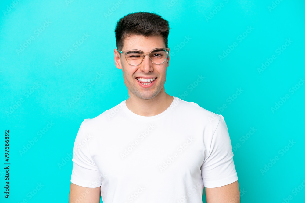 Obraz premium Young caucasian man isolated on blue background With glasses and happy expression
