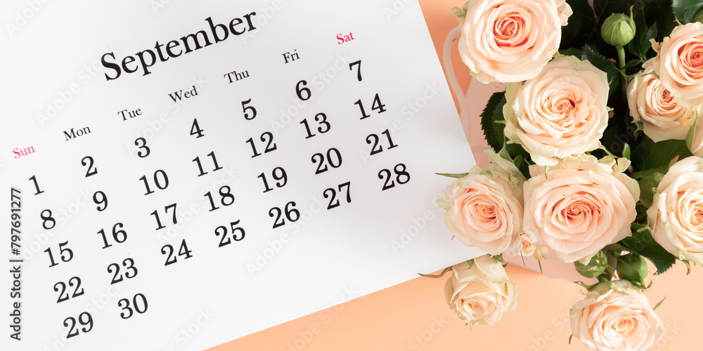 Fototapeta premium Flat desk paper calendar for September 2024, top view. Pale delicate roses on a beige background.