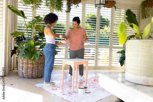 Mature biracial mother, adult daughter paint furniture in an upcycling project at home