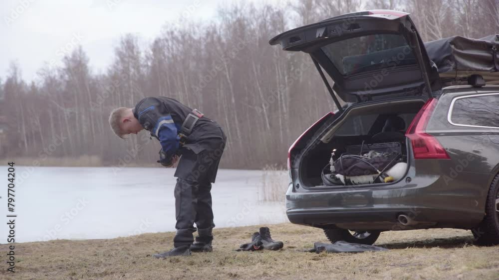 Ice diver in drysuit gearing up from his car trunk next to iced lake Ice diver in drysuit gearing up from his car trunk next to iced lake