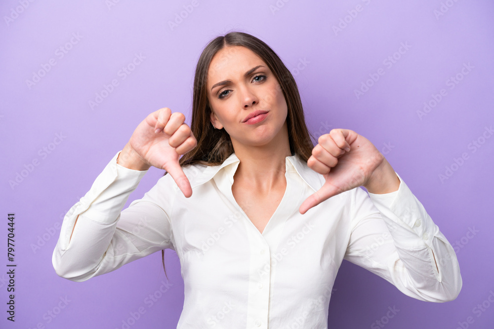 Young caucasian woman isolated on purple background showing thumb down with two hands Young caucasian woman isolated on purple background showing thumb down with two hands