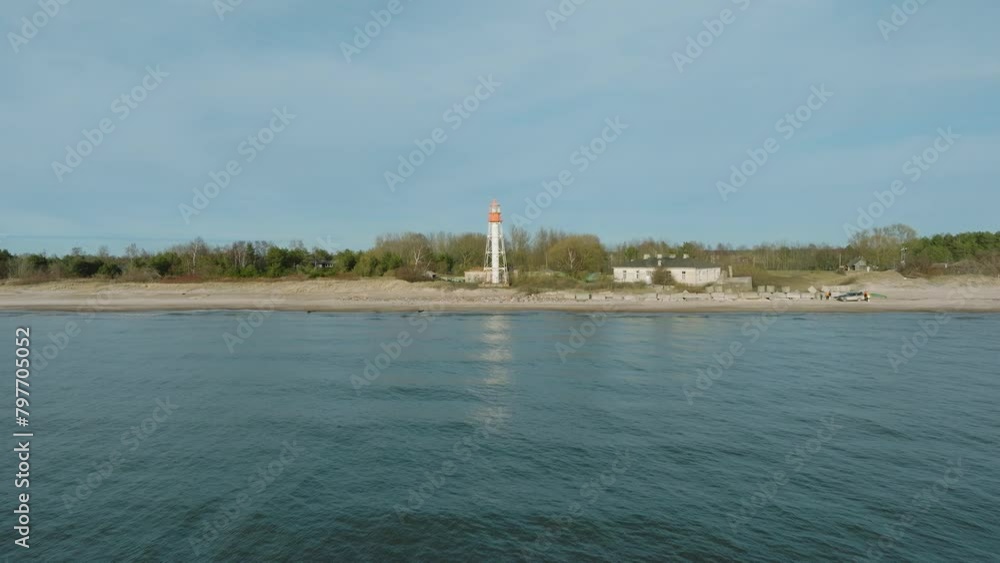 Aerial establishing view of white colored Pape lighthouse, Baltic sea coastline, Latvia, white sand beach, large waves crashing, sunny day with clouds, wide drone shot moving forward, ascending Aerial establishing view of white colored Pape lighthouse, Baltic sea coastline, Latvia, white sand beach, large waves crashing, sunny day with clouds, wide drone shot moving forward, ascending