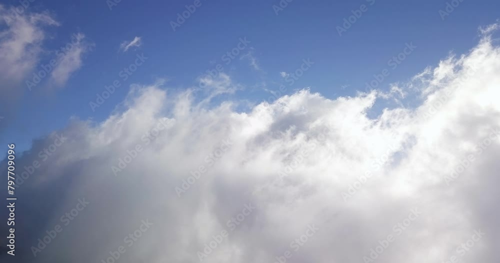 Billowing white clouds grow wispy tendrils reaching up into blue sky Billowing white clouds grow wispy tendrils reaching up into blue sky