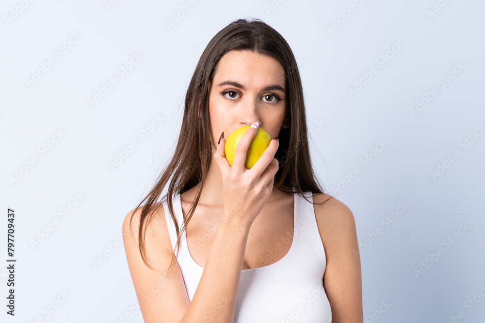 Young woman over isolated blue background eating an apple Young woman over isolated blue background eating an apple