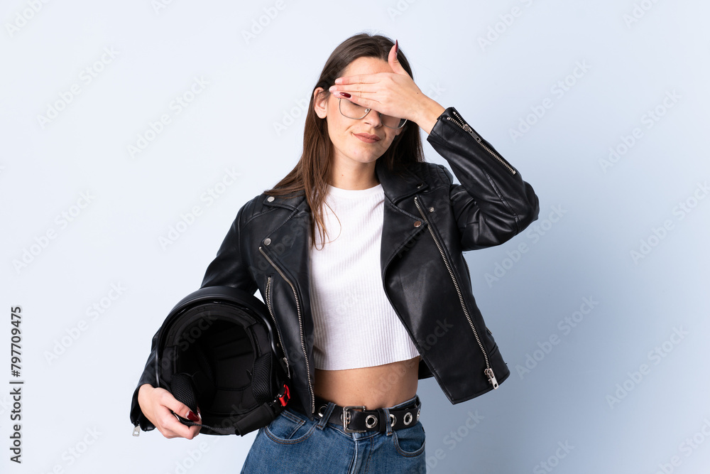 Young woman holding a motorcycle helmet over isolated blue background covering eyes by hands Young woman holding a motorcycle helmet over isolated blue background covering eyes by hands
