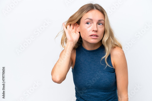Young Russian woman isolated on white background listening to something by putting hand on the ear