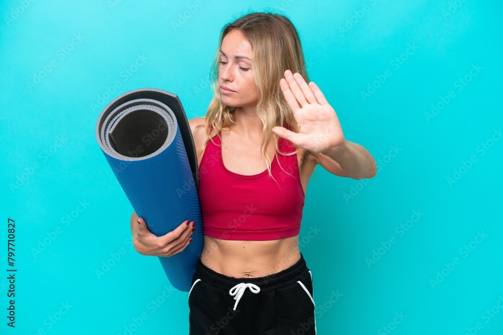 Young sport Russian woman going to yoga classes while holding a mat isolated on blue background making stop gesture and disappointed Young sport Russian woman going to yoga classes while holding a mat isolated on blue background making stop gesture and disappointed
