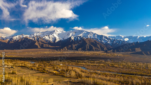 Panoramic view of Ladakh valley with blue Indus River flowing in the middle and snowcapped mountain peaks in the background.   photo
