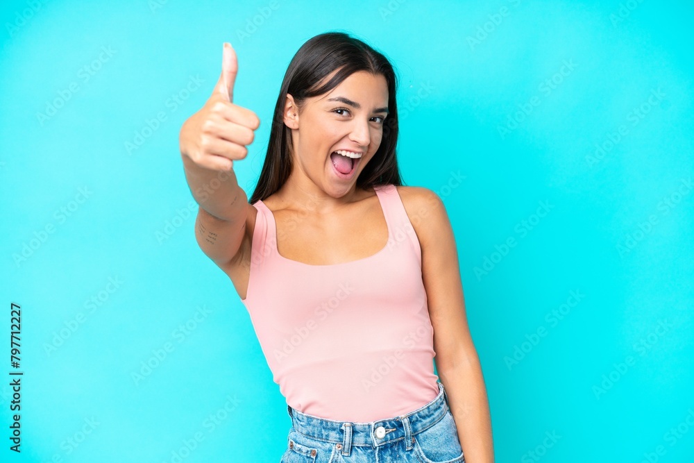 Young caucasian woman isolated on blue background with thumbs up because something good has happened Young caucasian woman isolated on blue background with thumbs up because something good has happened