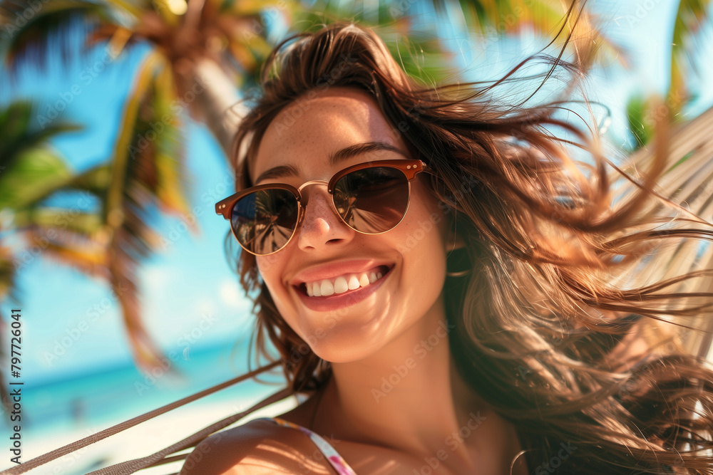 Close-up shot of a joyful woman with sunglasses, lying comfortably on a hammock with palm trees swaying in the breeze behind her