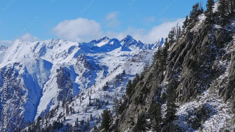 Drone shot of evergreen trees on rocky mountains covered with snow against blue sky on a sunny day Drone shot of evergreen trees on rocky mountains covered with snow against blue sky on a sunny day