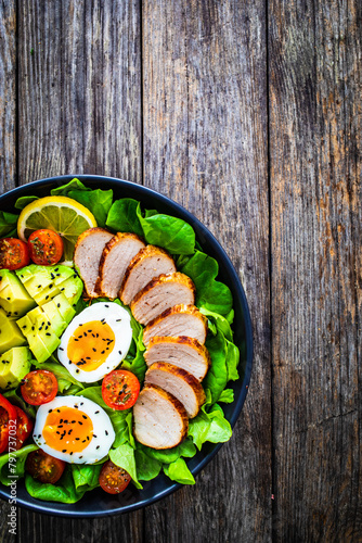 Tasty salad - roasted veal loin, avocado, boiled eggs and fresh vegetables on wooden table
 photo