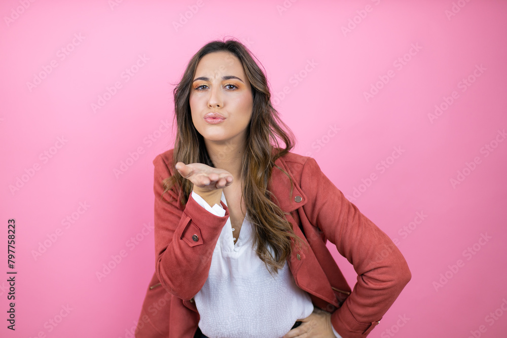 Young beautiful woman wearing casual jacket over isolated pink background looking at the camera blowing a kiss with hand on air being lovely and sexy. Love expression. Young beautiful woman wearing casual jacket over isolated pink background looking at the camera blowing a kiss with hand on air being lovely and sexy. Love expression.