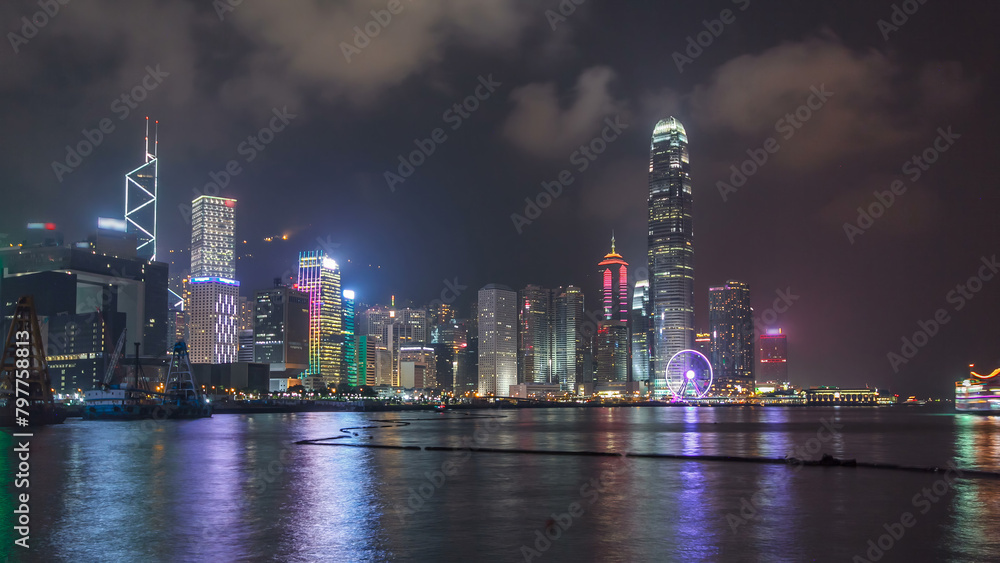 Hong Kong city skyline at night over Victoria Harbor with cloudy sky and urban skyscrapers timelapse hyperlapse.