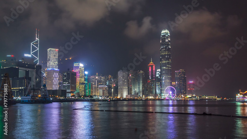 Hong Kong city skyline at night over Victoria Harbor with cloudy sky and urban skyscrapers timelapse hyperlapse.