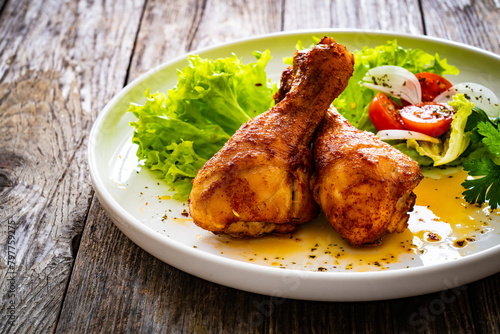 Roast chicken drumsticks with lettuce and tomatoes on wooden table
 photo
