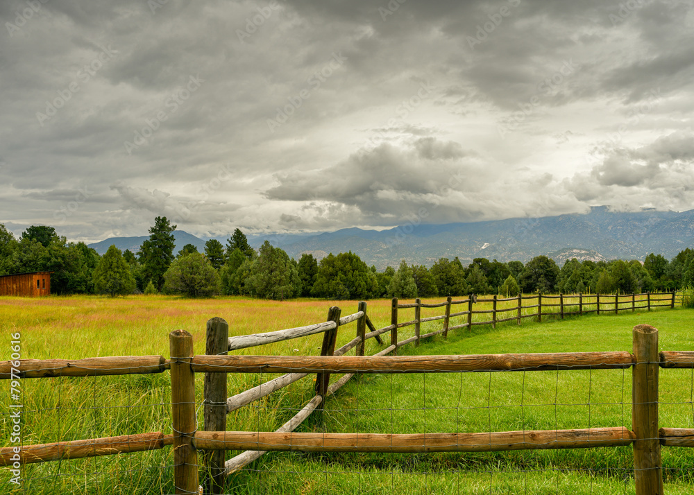 Rural Colorado landscape with split rail fence, open pastures, and dramatic skies