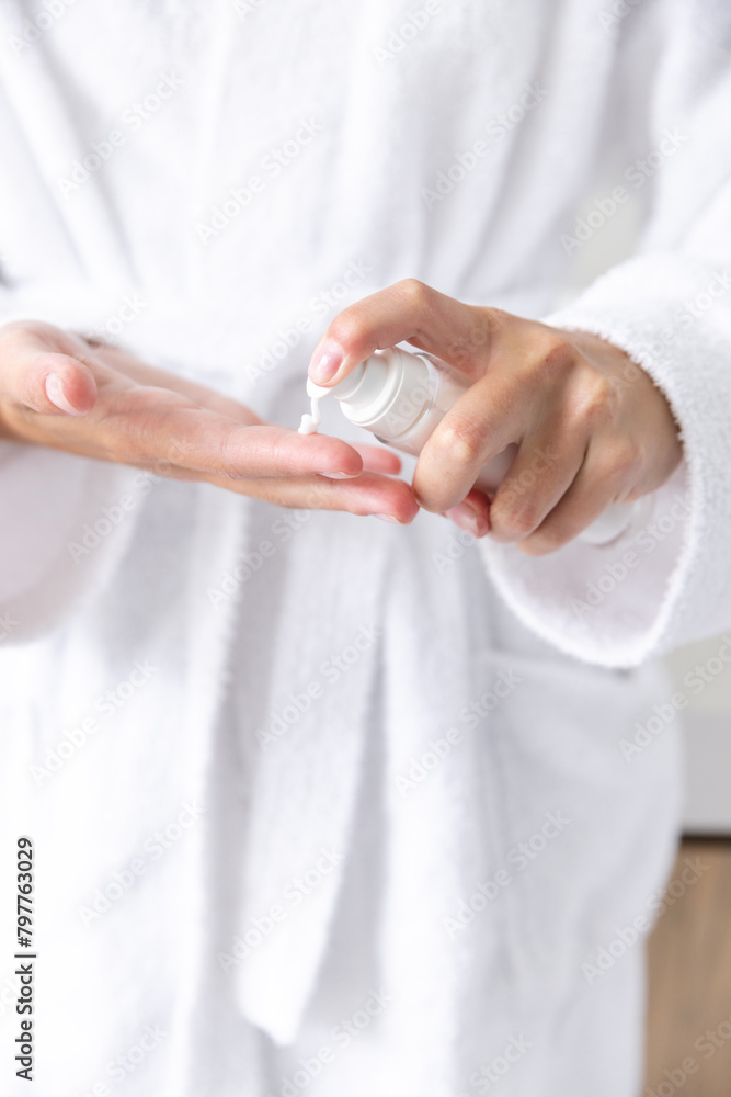 A young Caucasian woman in white robe applying lotion to her hands at home, copy space A young Caucasian woman in white robe applying lotion to her hands at home, copy space