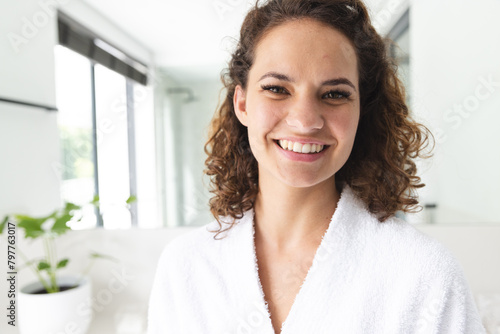 Caucasian young woman wearing white robe, smiling in bathroom photo