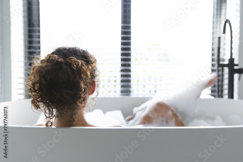 A young Caucasian woman relaxing at home in bathtub, enjoying alone time, copy space photo