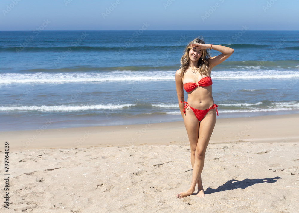 Fototapeta premium Smiling woman in red bikini posing on a sunny beach.