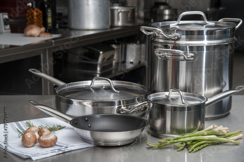 Stainless steel cookware set with fresh vegetables on a chef's table