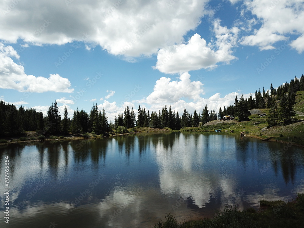 Evergreen trees encircle a serene lake under a clear blue sky