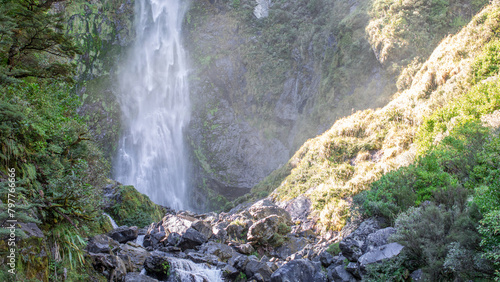 Sunlit waterfall cascades through lush NZ foliage, a serene Arthur's Pass gem © Виктория Попова