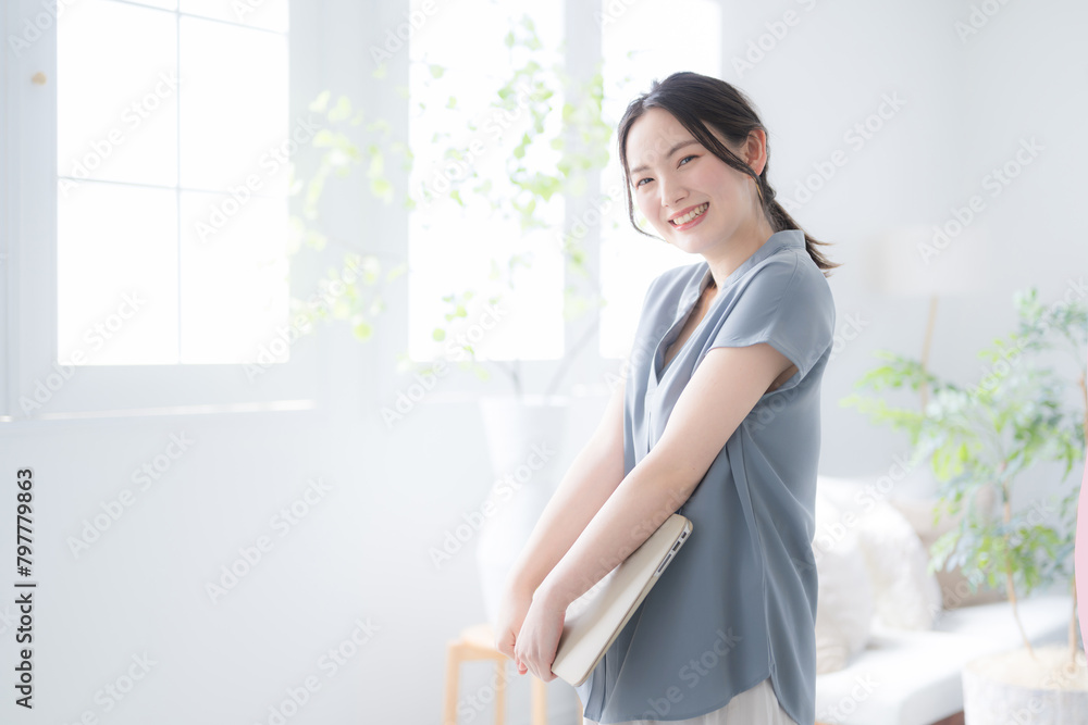 綺麗なオフィスの窓辺でノートパソコンを持つ美しい女性 パソコンを抱えるカメラ目線で笑顔 綺麗なオフィスの窓辺でノートパソコンを持つ美しい女性 パソコンを抱えるカメラ目線で笑顔