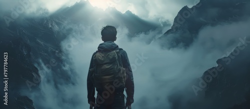 The back of a man with a bag on his back, standing on a high mountain, looking down,mysterious content,Dramatic light, generated with AI photo