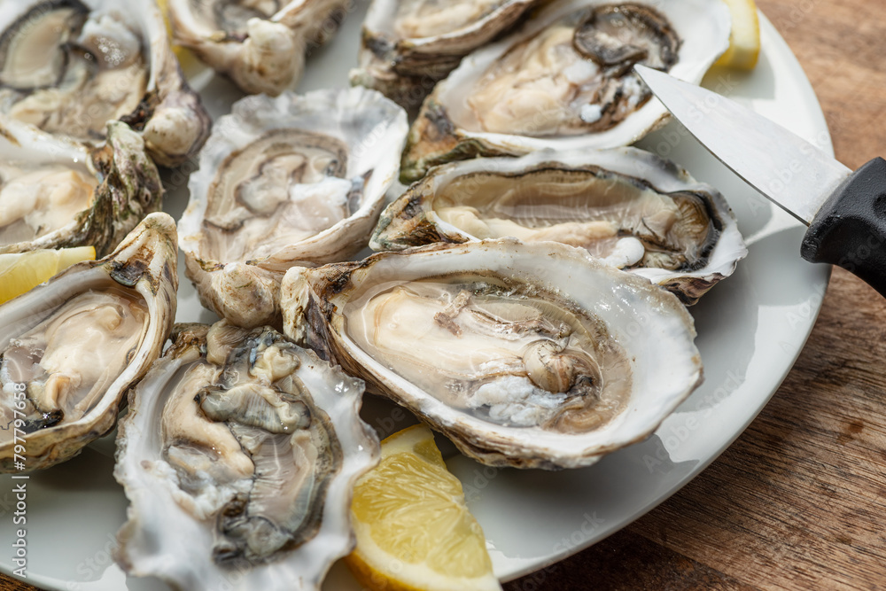 Opened raw oysters with sauce and lemon slices on plate on wooden table. Top view. Opened raw oysters with sauce and lemon slices on plate on wooden table. Top view.
