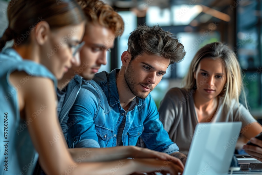 A group of young adults are working together on a laptop in an office. A group of young adults are working together on a laptop in an office.