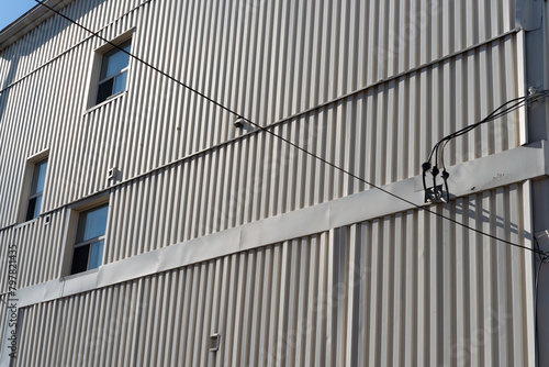 side of a building clad in corrugated sheet metal with wires and window openings