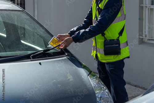 Traffic warden in the UK puts a parking fine ticket on the window of a car photo