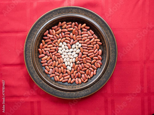 A Heart made out of Healthy Pinto Beans in a field of Kidney Beans, arranged on a Brown Plate on a Red tablecloth.