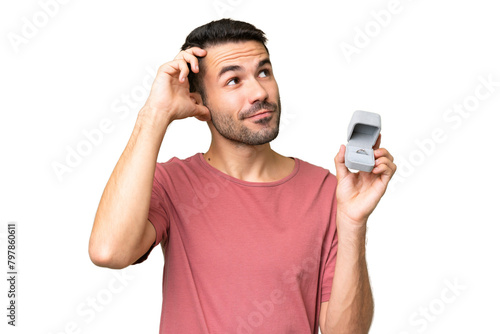 Young handsome caucasian man holding a engagement ring over isolated background having doubts and with confuse face expression © luismolinero