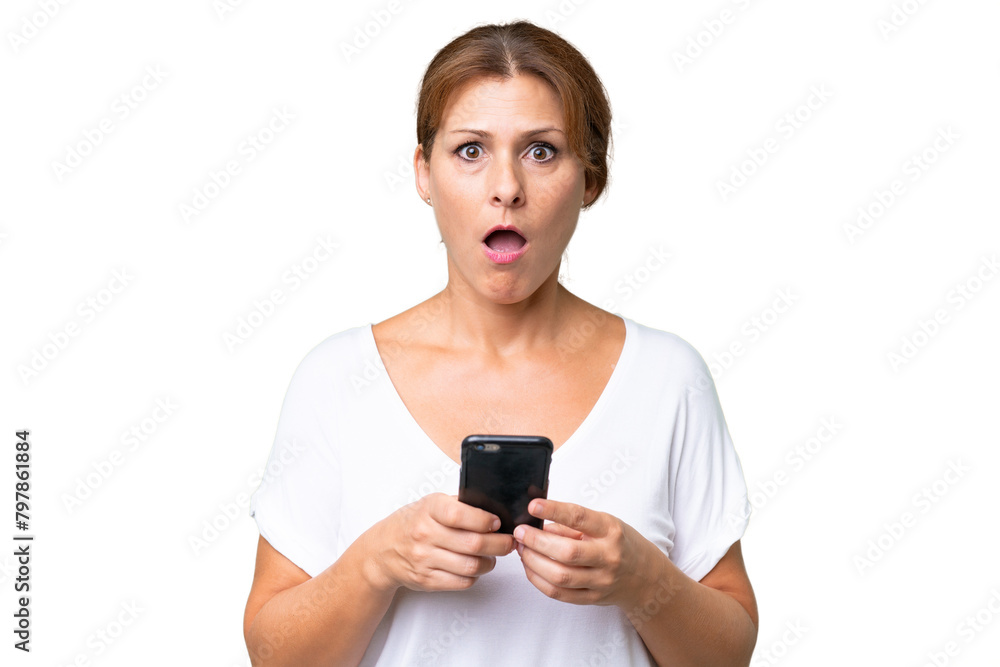 Middle-aged caucasian woman over isolated background looking at the camera while using the mobile with surprised expression Middle-aged caucasian woman over isolated background looking at the camera while using the mobile with surprised expression
