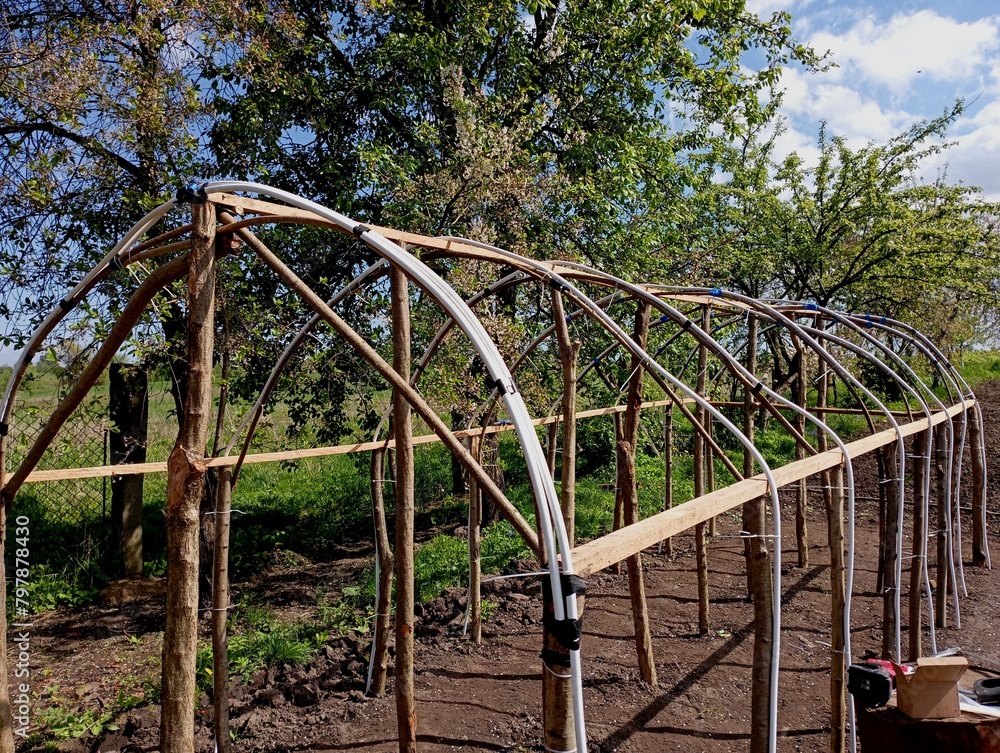 A frame made of improvised materials of a home-made greenhouse. Construction of a greenhouse from wood. the topic of growing vegetables in greenhouses.