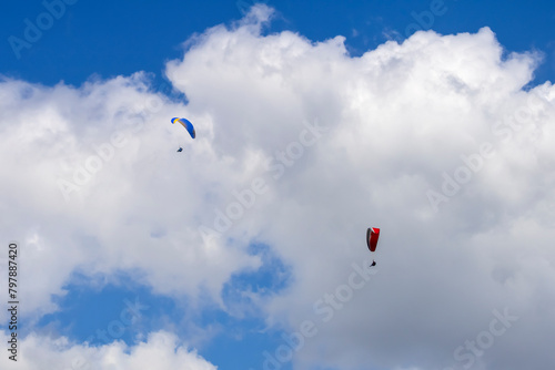 Two paragliders in blue sky with white gray clouds