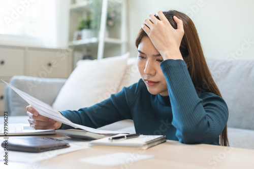 Stressed asian young employee, business woman calculate tax, income and expenses, hand looking bills of credit card for payment or payday on table at home office. Financial, finance people concept.
