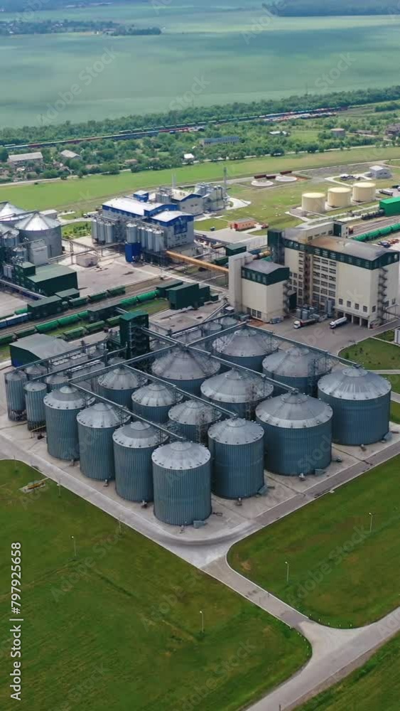 Modern factory among fields. Grain elevators for keeping agricultural products. Grain storage tank in the countryside. Aerial view. Vertical video Modern factory among fields. Grain elevators for keeping agricultural products. Grain storage tank in the countryside. Aerial view. Vertical video