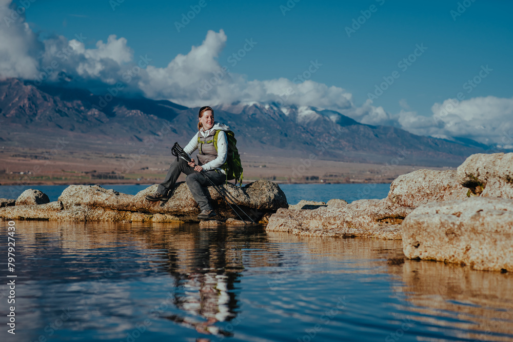 Woman tourist sits on a rock in lake on mountains background and looking away