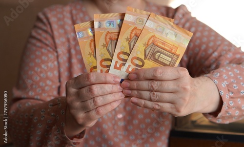Financial calculations in the form of a close-up on the hands of a European woman in a pink shirt, counting money into a pack of 50 euros spread out like a fan