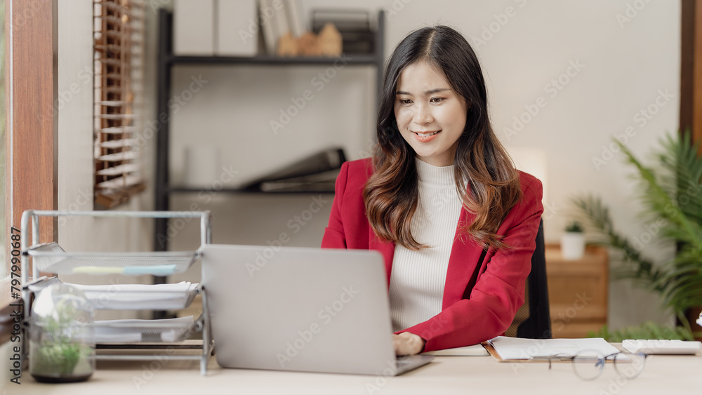 Asian woman using laptop computer and working at office with calculator document on table, planning to analyze financial report, business plan, financial investment Asian woman using laptop computer and working at office with calculator document on table, planning to analyze financial report, business plan, financial investment