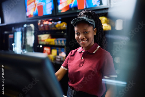 Happy black concession stand worker using computer in movie theater. photo